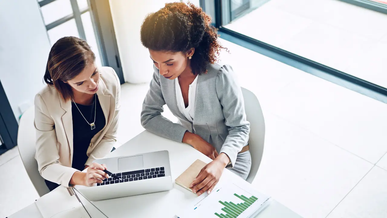 Due professioniste analizzano insieme dati HR al laptop in ufficio, con report e grafici sulla scrivania