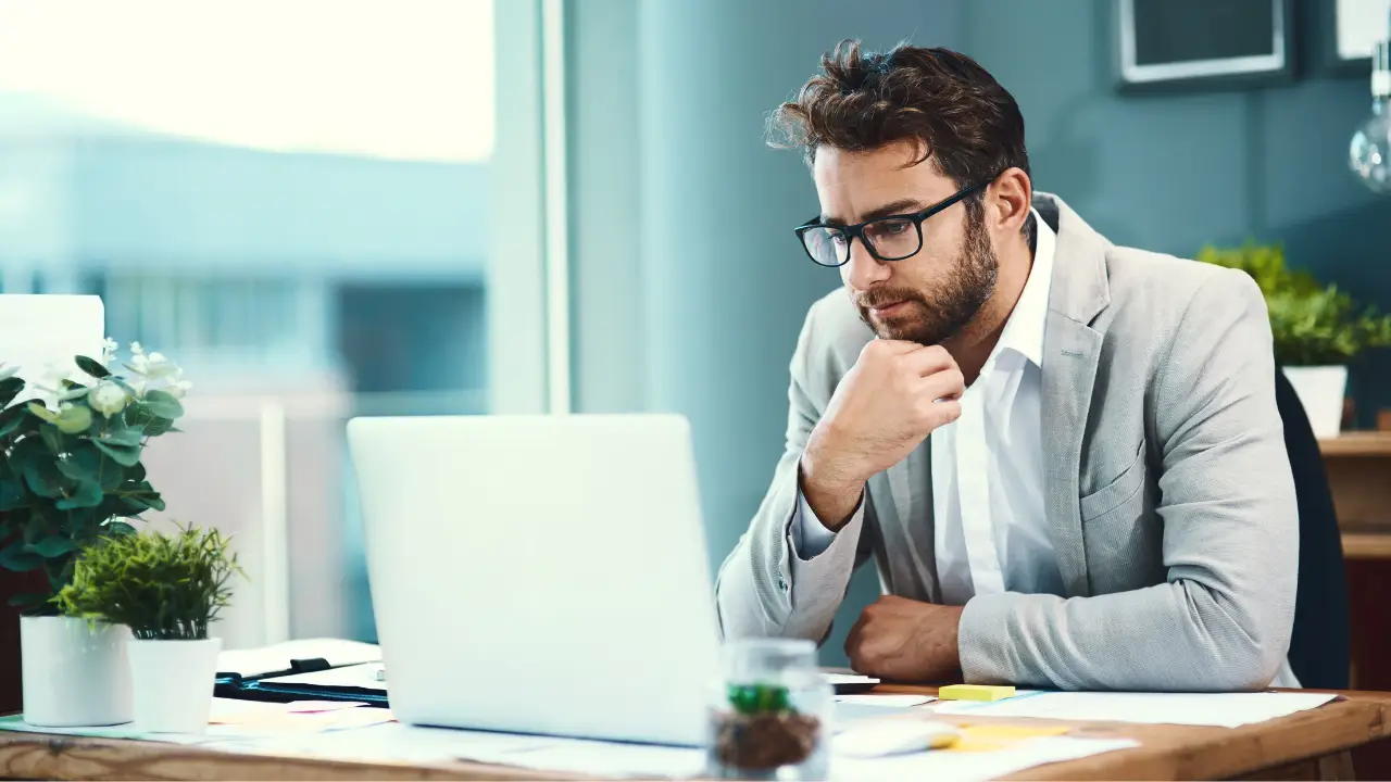 Professionista con occhiali seduto alla scrivania guarda il laptop concentrato, mentre verifica le nuove regole del TFR3